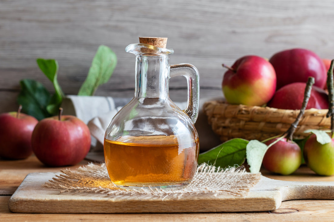 glass carafe of apple cider vinegar on wooden table with apples in the background