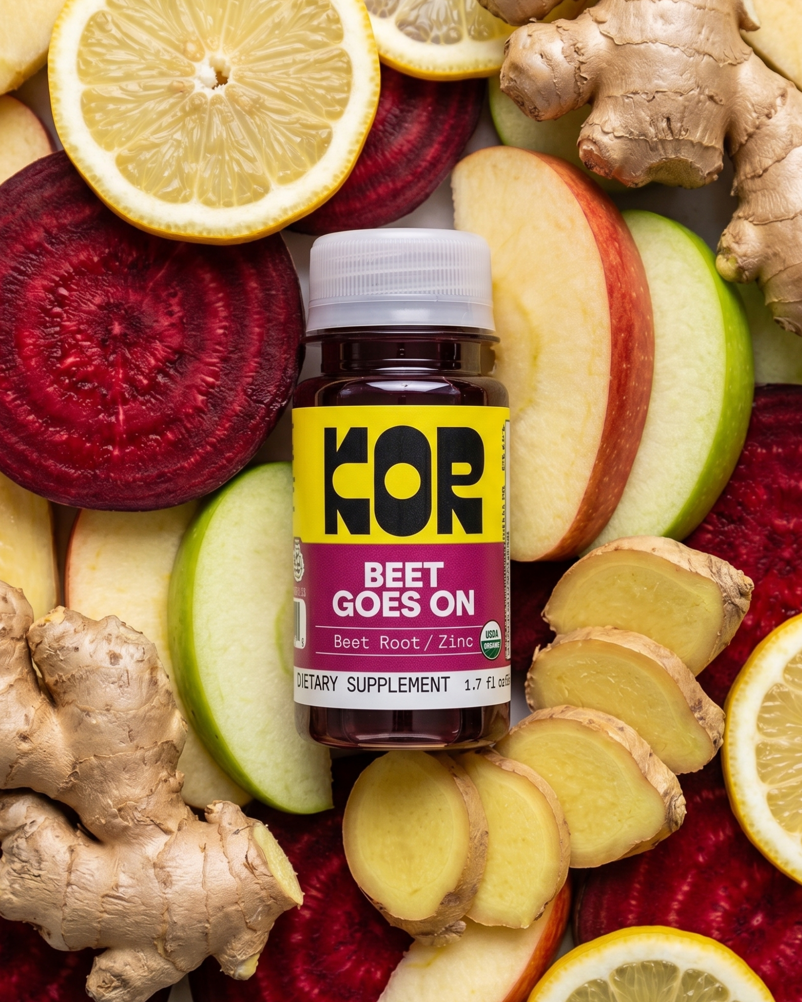 A bottle of KOR Beet Goes On dietary supplement centered on a flat-lay background of sliced beets, lemon, apple, and ginger.